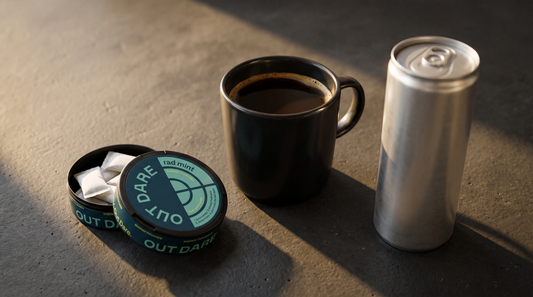 Open OutDare Energy Pouches can, black coffee mug, and bare silver cylinder on dark concrete