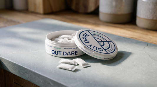 Open nicotine pouch can with white pouches beside it on a pale honed slate worktop