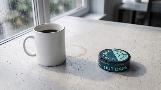 An OutDare caffeine pouch can beside a half-drunk coffee mug on a pale concrete office worktop