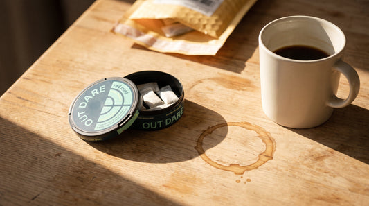 Caffeine pouches can on a well-used desk, coffee mug displaced to reveal a dried ring stain