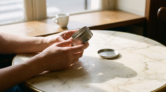 Adult hands holding an open nicotine pouch can on a marble café table