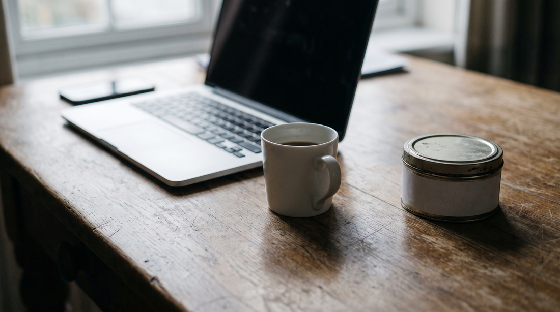 Open laptop on a wooden desk beside a small round pouch can in grey morning light