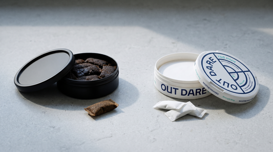 Open brown snus can beside an open white nicotine pouch can on pale grey stone, nicopods comparison