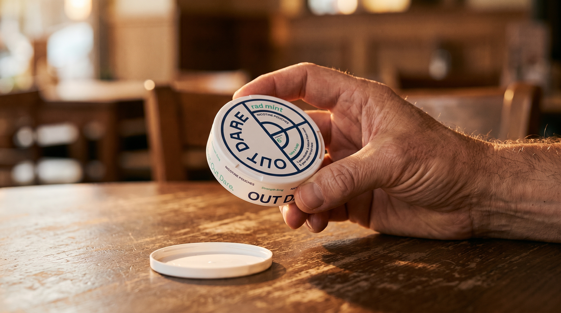 Adult hand holding an open nicopods can above a warm wooden café table