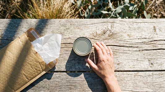 Nicotine pouch can lifted from a postal mailer on a sun-bleached outdoor timber table