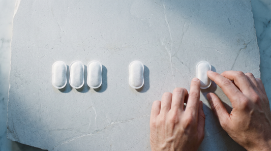 Five white nicotine pouches laid in a diminishing row on pale stone, an adult hand beside them