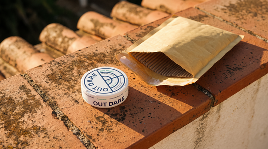 Nicotine pouch can beside an opened shipping envelope on sun-lit terracotta tiles