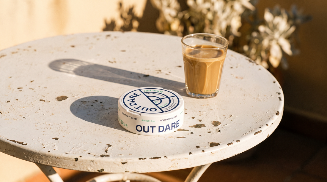 OutDare nicotine pouches can on a sunny outdoor café table beside a cortado, Spanish terrace