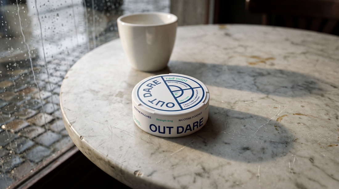 Small round nicotine pouch can resting on a worn marble café table in Belgian daylight