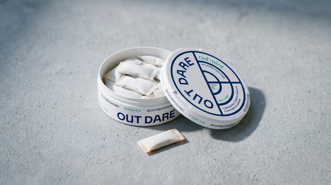 Open nicotine pouch can showing white pouches inside with one resting on pale grey concrete