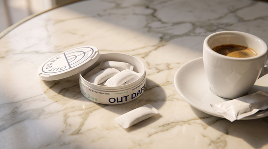 Open nicotine pouch can beside a small espresso on a marble café table