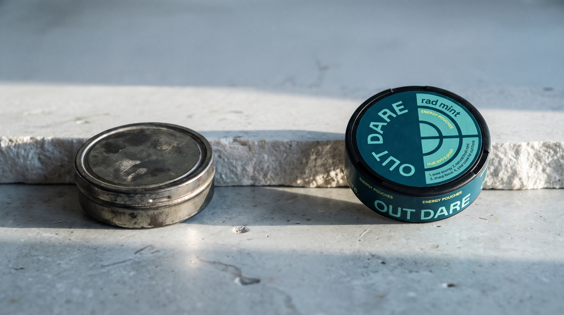Worn dark snus can beside a round flat caffeine energy pouch can on pale grey stone