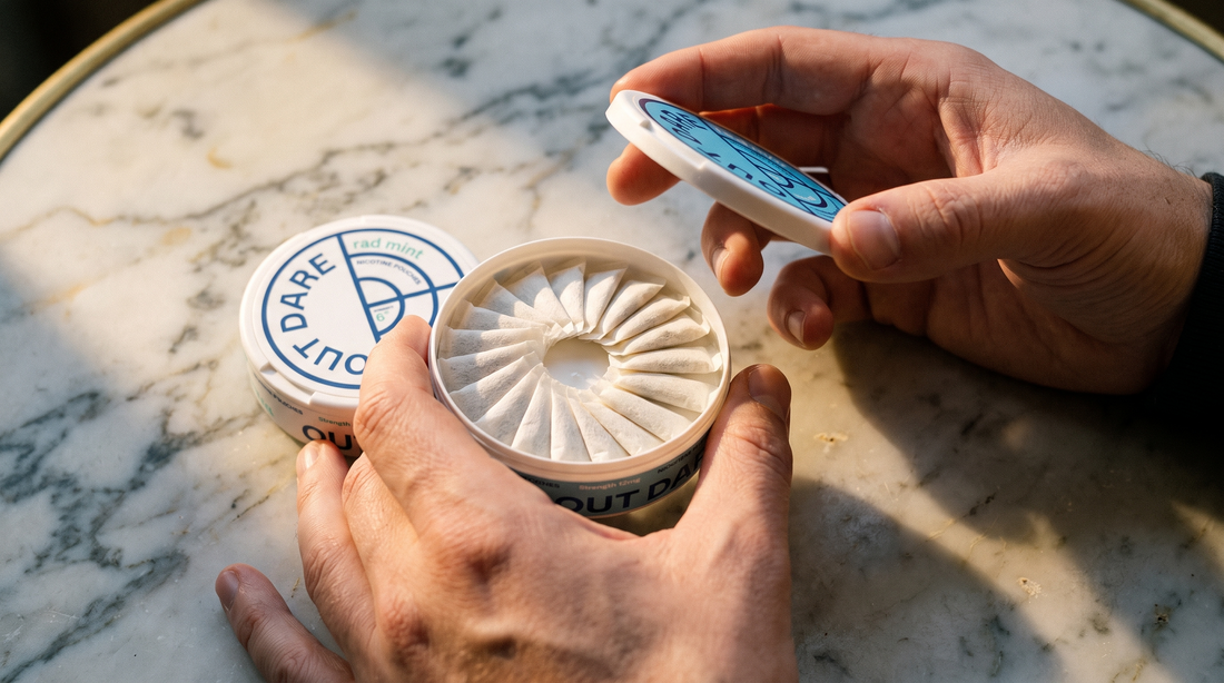Two adult hands opening a round flat nicotine pouch can to reveal white pouches inside