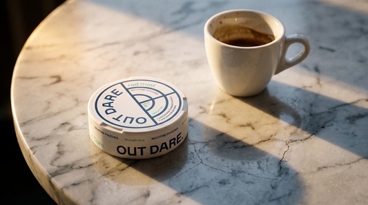 An OutDare nicotine pouch can on a marble café table beside an espresso cup