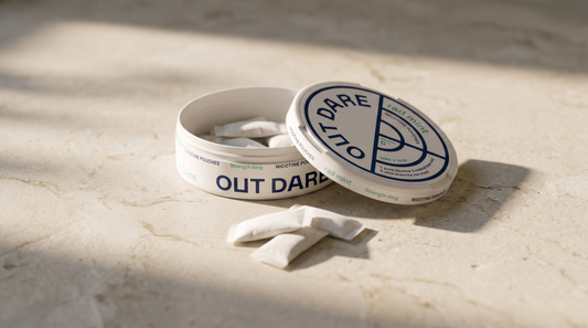 An open nicotine pouch can with white pouches on a pale stone surface