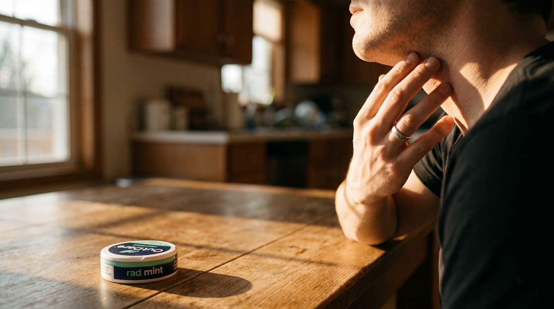 Adult at a kitchen table, hand raised to jaw, sensing why nicotine pouches burn