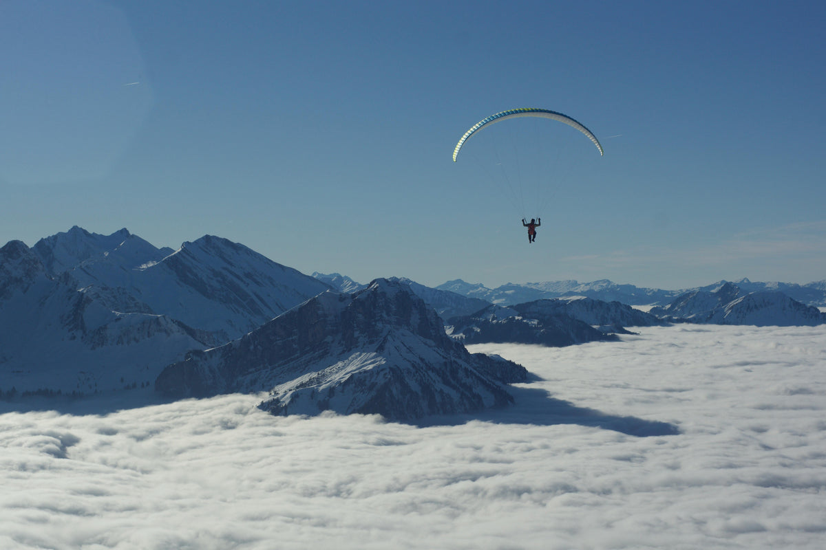 Paraglider flying over the mountains above a sea of clouds